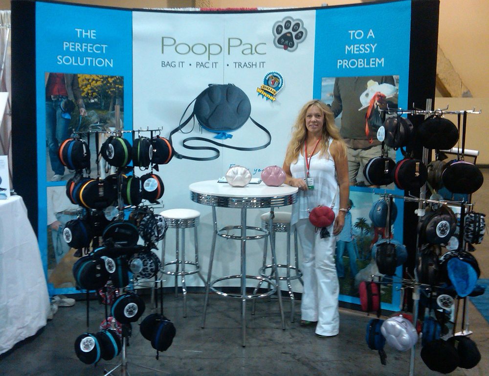 Susan Davidson at the PoopPac trade show booth, surrounded by PoopPac cases in many colors